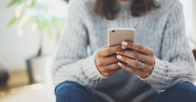A woman wearing a sweater texts on her smart phone